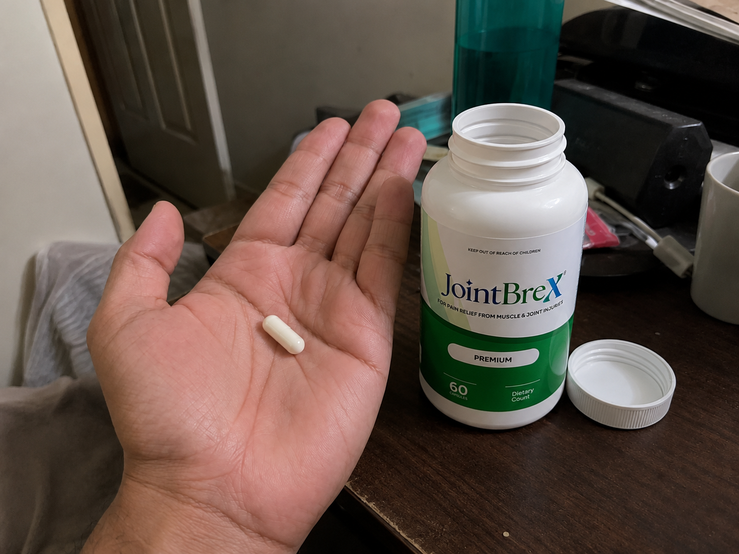 Hand holding a JointBrex capsule next to the open bottle